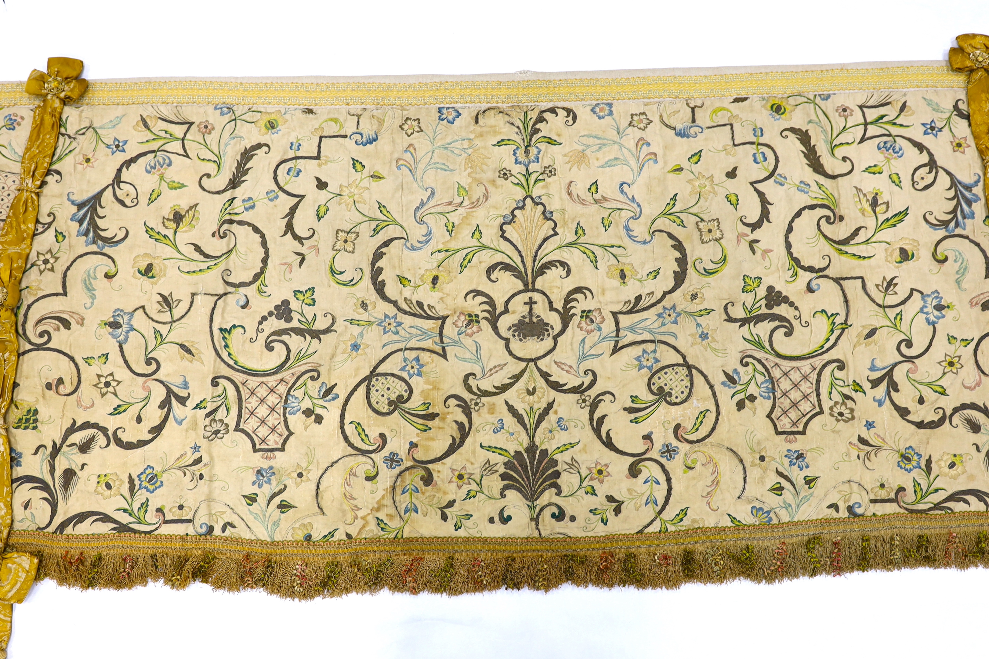 A mid-18th century Continental silk embroidered altar cloth, embroidered with polychrome silks and silver metallic threads in an all-over floral design on cream silk with ornate silk tasselling, (the damask tie backs add